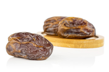 Group of three whole dry brown date fruit on bamboo coaster isolated on white background