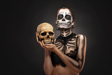 Halloween girl with skull makeup for Halloween on a black background holds a human skull in her hands