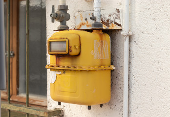 Old yellow gas meter hanging on a wall outdoors.