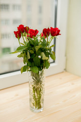 Bouquet of red roses in glass vase with heart on windowsill background
