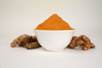 Turmeric powder in a white cup and isolated turmeric root on a white background is used as a tonic for body and food ingredients.