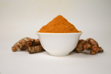Turmeric powder in a white cup and isolated turmeric root on a white background is used as a tonic for body and food ingredients.