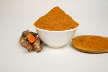 Turmeric powder in a white cup and isolated turmeric root on a white background is used as a tonic for body and food ingredients.