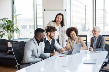 A team of professionals having a meeting in the conference room. They are cheerful and smiling. There are three women and two men.