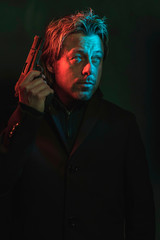 Man holding pistol next to his head. Illminated by red and blue light during the night.