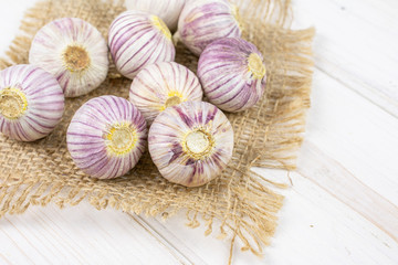 Obraz na płótnie Canvas Lot of whole fresh purple single clove garlic on natural sackcloth on white wood