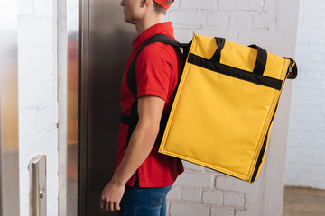 Cropped view of delivery man with thermo backpack standing near elevator