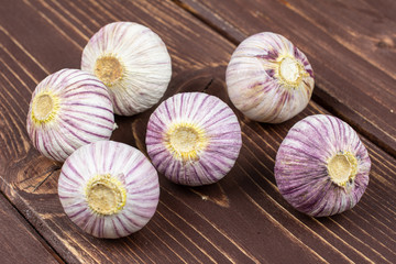 Group of six whole fresh purple single clove garlic on brown wood