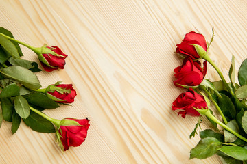 Red roses lie on a wooden table, frame decorated with flowers. There is a place for text.