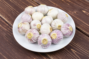 Lot of whole fresh purple single clove garlic on white ceramic plate on brown wood