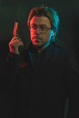 Man holding gun next to his head. Illminated by red and blue light.