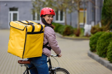 Side view of attractive courier with thermo backpack and bicycle smiling at camera on street