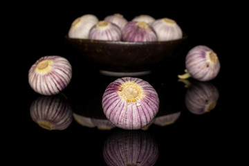 Lot of whole fresh purple single clove garlic in dark ceramic bowl isolated on black glass