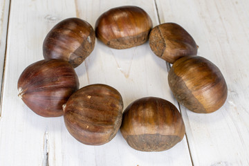 Group of seven whole edible brown chestnut circle on white wood