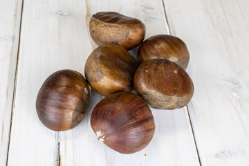 Group of six whole edible brown chestnut on white wood