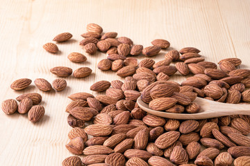Closeup almonds nut are poured from wooden spoon on sack and table.