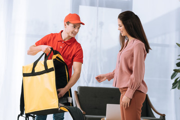 Smiling courier with thermo bag near attractive woman at home