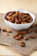 Closeup almonds nut are poured from white bowl on wooden table.