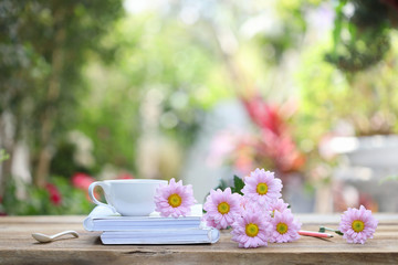 Obraz na płótnie Canvas White coffee cup with white notebook and pink pencil with pink Chrysanthemum flower on wooden table at outdoor 