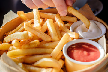 Appetizing French fries with sauce in a wooden dish, in natural light from the window.
