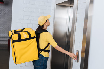 Side view of courier with thermo backpack pressing elevator button