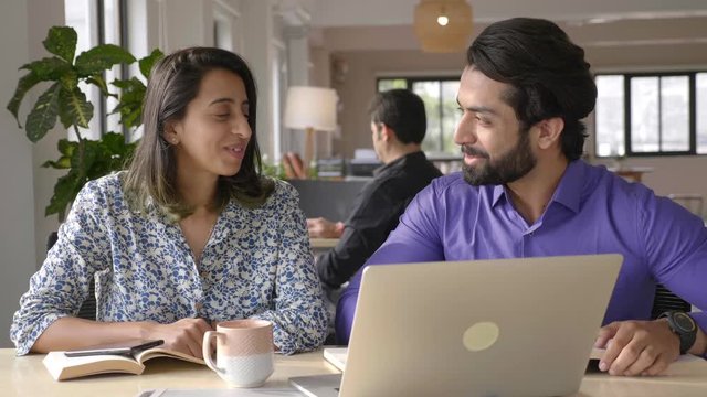 young businessman and a young female colleague discussing work with laptop at their workplace.they are working smiling and interacting cheerfully.