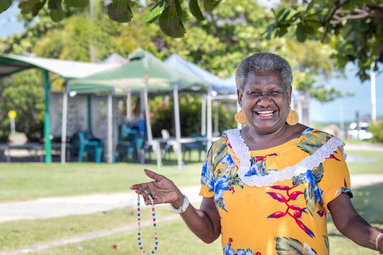 Portrait of a melanesian - australian mature woman smiling, showing the hand-made jewerly that she has made, outdoors.