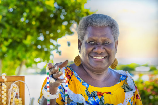 Portrait of a melanesian - australian mature woman smiling, showing the hand-made jewerly that she has made, outdoors.