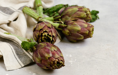 Obraz premium Fresh artichokes on a light stone table. . organic seasonal vegetables. artichoke recipe. selective focus