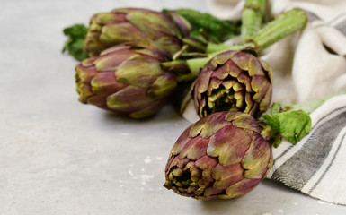 Obraz premium Fresh artichokes on a light stone table. . organic seasonal vegetables. artichoke recipe. selective focus