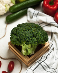 Fresh broccoli cabbage close-up on a wooden stand, in the background cucumbers, cauliflower, peppers, tomatoes.