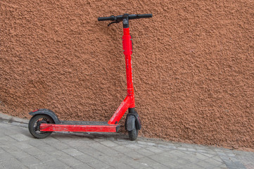 red scooter on a street leaning on a wall
