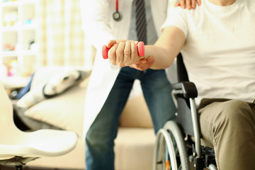 Male doctor helps lift dumbbell to disabled patient rehabilitation therapy concept. Process of recovering patients after severe injuries