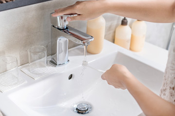 Dental care. Woman hands is holding toothbrush with toothpaste in bathroom, sink and running faucet in background