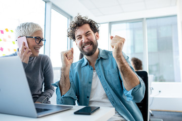 An employee happy to hear the good news about his promotion told by a senior colleague. The female colleague is talking on the phone.