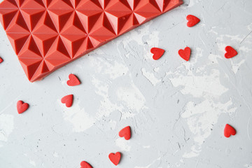 red chocolate bar, scattered small hearts on a white background. background for Valentine's day