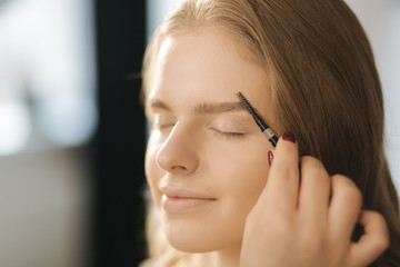 Makeup artist work in her beauty studio. Portrait of Woman applying by professional make up master. Beautiful make up artist start making a makeup for blond hair model