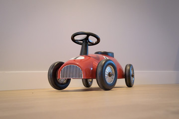 Retro toy car seen from front, against grey wall and on wooden floor