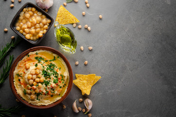 Flat lay view at Hummus in clay dish topped with olive oil, chickpeas and green coriander leaves on stone table served with ttortilla chips