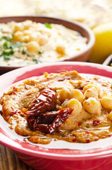 Fresh homemade Hummus in clay dish topped with olive oil, chickpeas, spices and sun dried tomatoes on stone table
