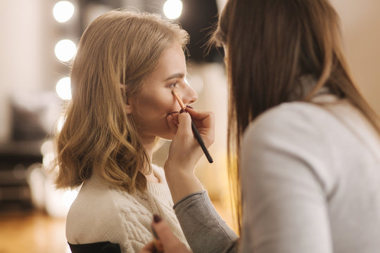Makeup artist work in her beauty studio. Portrait of Woman applying by professional make up master. Beautiful make up artist start making a makeup for blond hair model