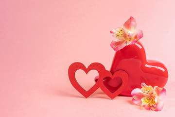Red vase shaped heart with flowers alstroemeria and two red wooden hearts on pink. Valentines day festive background.