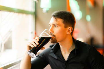 A handsome middle-aged man in a bar. The boy enjoys a dark beer. There is a pleasant atmosphere for fun.