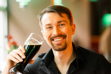 A handsome middle-aged man in a bar. The boy enjoys a dark beer. There is a pleasant atmosphere for fun.