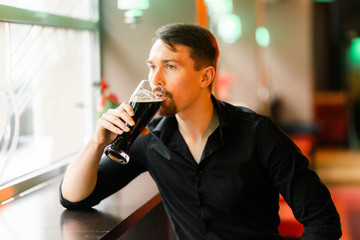 A handsome middle-aged man in a bar. The boy enjoys a dark beer. There is a pleasant atmosphere for fun.