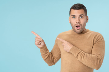 Fototapeta premium Surprised man pointing finger away at copy space isolated on blue background