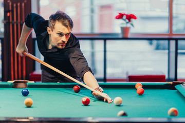 Fototapeta premium A man tries his hand at playing billiards. He is accompanied by various emotions, satisfaction, anger, frustration, focus. The décor of the place where the game gives the fun a unique character.