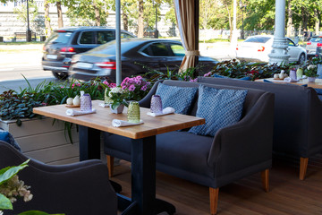 Empty veranda summer cafe in the city. Blue sofas with pillows, wooden table with dishes.