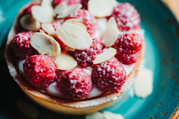 Raspberry tartlet dessert with almond flakes on a blue ceramic plate. Close-up view.