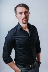 Fototapeta premium Photo of a handsome man with a coolly stylized scrub and hairstyle. Photo taken in a photo studio on a gray background. The man tries to express his emotions with gesticulation and mimics.